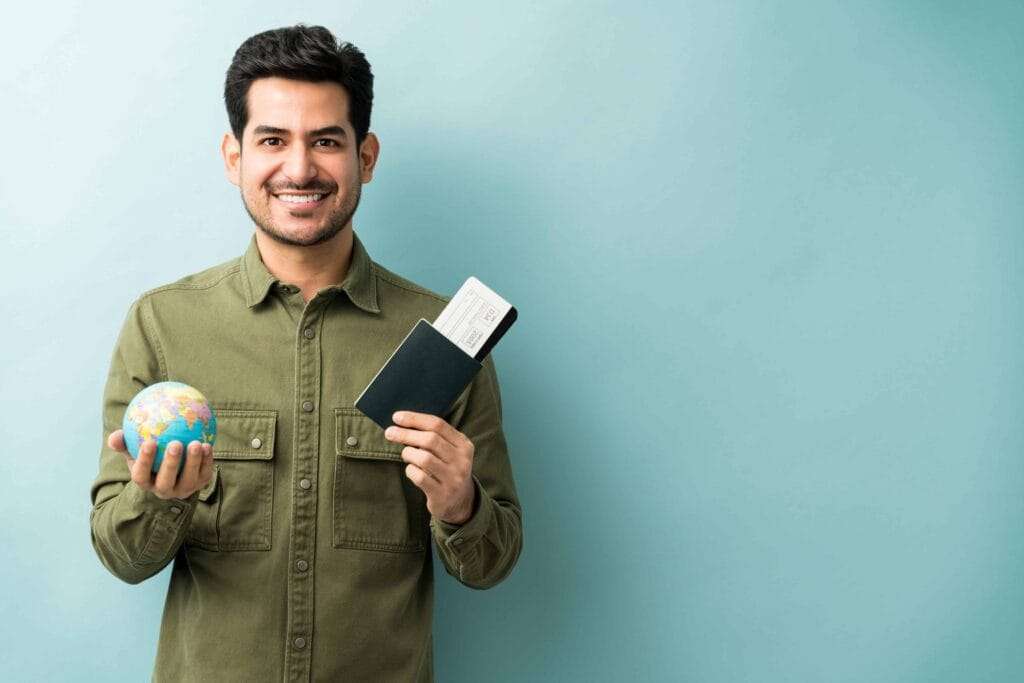 Freezone Company Formation in Dubai 11 happy young man holding passport boarding pass with globe while standing against blue background 1